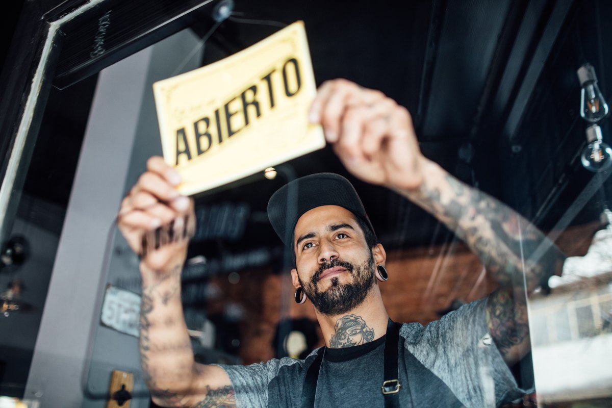 A shop owner holding up an Abierto sign in his storefront window