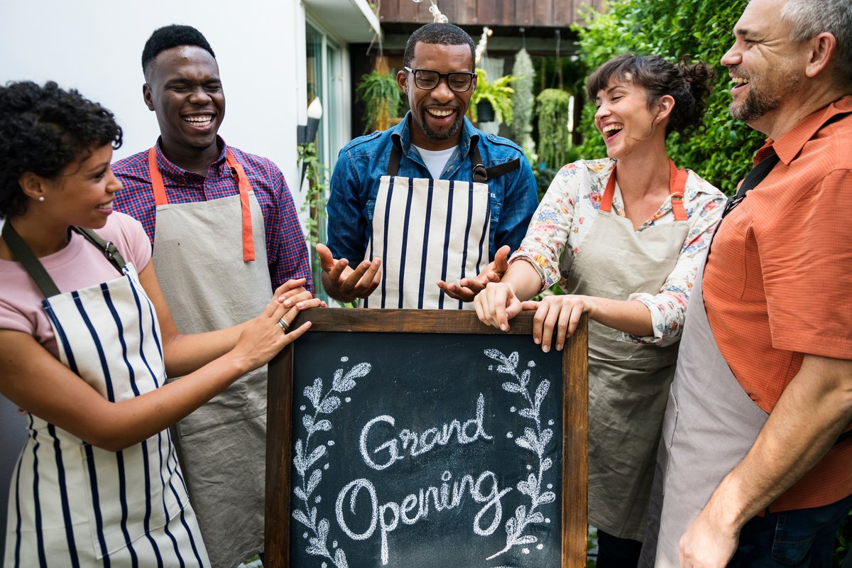 A team of aprons-clad small business owners celebrating a grand opening with a chalkboard sign